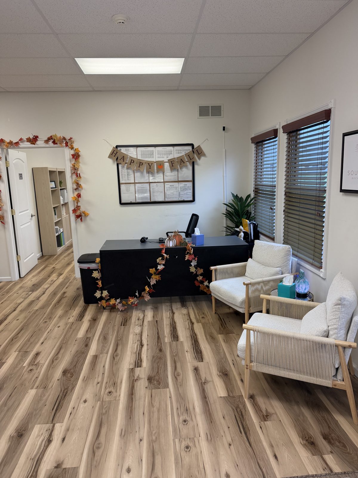 Front desk in the waiting area, with a notice board behind it and two armchairs by the windows